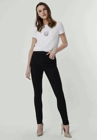Λευκό T-shirt με γραφικό σχέδιο, σε συνδυασμό με εφαρμοστά μαύρα κολάν και μπεζ ψηλοτάκουνα. Απαλή ύφανση, μινιμαλιστικός σχεδιασμός.