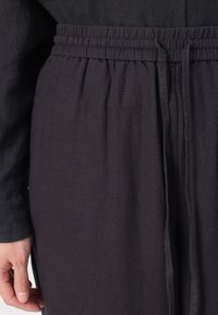 Black linen pants with an elastic waistband, featuring a relaxed fit and subtle texture for comfort. Drawstring detail at the waist.