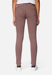 Jeans rosa ajustados de denim, con bolsillos traseros y una cintura de altura media, combinados con zapatillas blancas detalladas con acentos negros.