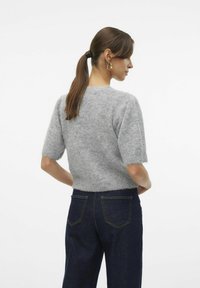 Grauer kurzärmeliger Pullover aus weichem Strickmaterial, mit Rundhalsausschnitt und leicht ausgefransten Kanten, kombiniert mit dunkelblauen Jeans.