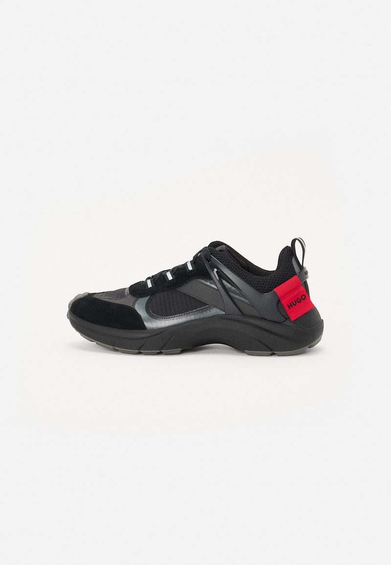 Black athletic shoe featuring mesh and suede materials, a rounded toe, chunky sole, and a red accent on the heel with the brand name.