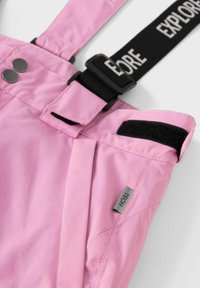 Salopette impermeabile rosa con spallacci neri regolabili, etichettati "EXPLORE". Caratteristiche includono bottoni metallici, accenti in velcro e tasche laterali.