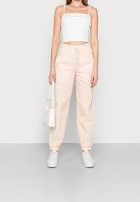 Lehké, broskvové tepláky s elastickým pasem a manžetami, spárované s bílým cropped topem a bílými teniskami.