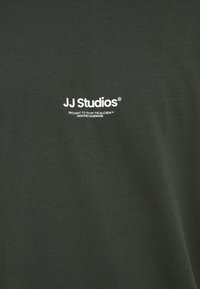 T-shirt in cotone verde scuro con scritta bianca "JJ Studios" e testo aggiuntivo sotto. Tessuto morbido con vestibilità casual.
