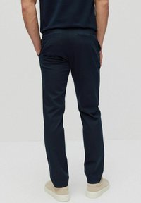 Donkerblauwe broek met een gladde textuur, voorzien van twee achterzakken en een op maat gemaakte pasvorm, gecombineerd met lichtgekleurde, eenvoudige sneakers.