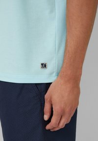 Jasnoniebieska koszulka z krótkim rękawem z małym haftowanym logo na lewym dolnym brzegu, noszona z granatowymi szortami o fakturowanej strukturze.