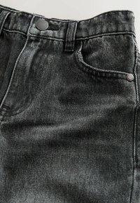 Blugi negri din denim cu finisaj uzat. Au un singur buzunar frontal, cusături cusute și un nasture metalic la talie.