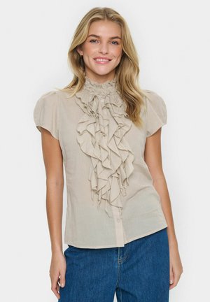 Helle beige Bluse mit hohem Rüschenausschnitt, kurzen Ärmeln und Knopfverschluss. Weiche Textur, mit geschichteten Rüschen vorne.
