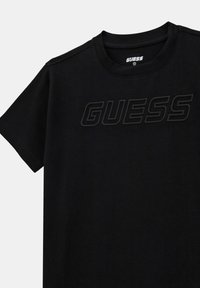 Svart bomullströja med rundad halsringning och korta ärmar. Har en texturerad "GUESS"-logotyp i en något mörkare nyans. Mjuk tyg.