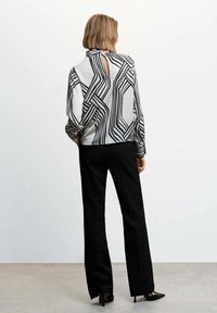 Blouse à motifs noir et blanc avec un col montant et une ouverture en forme de trou de serrure dans le dos, associée à un pantalon noir et des talons pointus. Texture lisse et soyeuse.