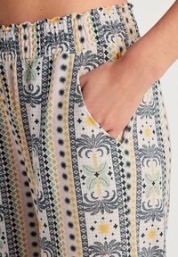 Cotton pants with a stretchy waistband, featuring a multi-colored pattern of palm trees, suns, and geometric designs. Includes side pockets.