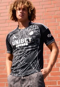 Svart kortermet sports skjorte med hvite detaljer og mønstre, med rund hals og sponsorlogoer tydelig vist.