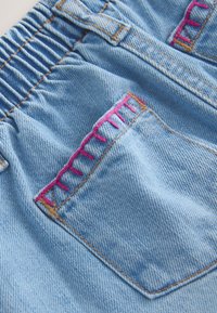 Svetlomodro denim blago z žepom, ki ima rožnate dekorativne šive, in elastičnim pasom z nabranim blagom.