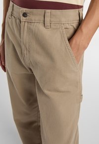 Béžové bavlněné chinos kalhoty se rovný fit, s bočními kapsami a texturovanou tkaninou. Pas obsahuje kovový knoflík a poutka na pásek.