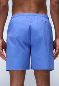 Șorturi de baie de un albastru deschis, fabricate dintr-un material texturat și ușor. Prezintă un tiv elastic și un mic buzunar pe spate.
