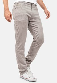 Pantalons rayés, couleur marron clair, fabriqués en tissu doux, avec une coupe ajustée, des poches latérales et une fermeture éclair. Accentué par des coutures subtiles.