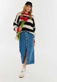 Preveľký pletený sveter s čierno-bielymi pruhmi a červenými akcentmi, skombinovaný s dlhou džínsovou sukňou so zipsom vpredu a rozparkom.