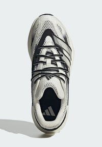 Vita och svarta sportskor med meshtopp, texturerade paneler, kontrasterande ränder och en logotyp på innersulan. Svarta snören finns.