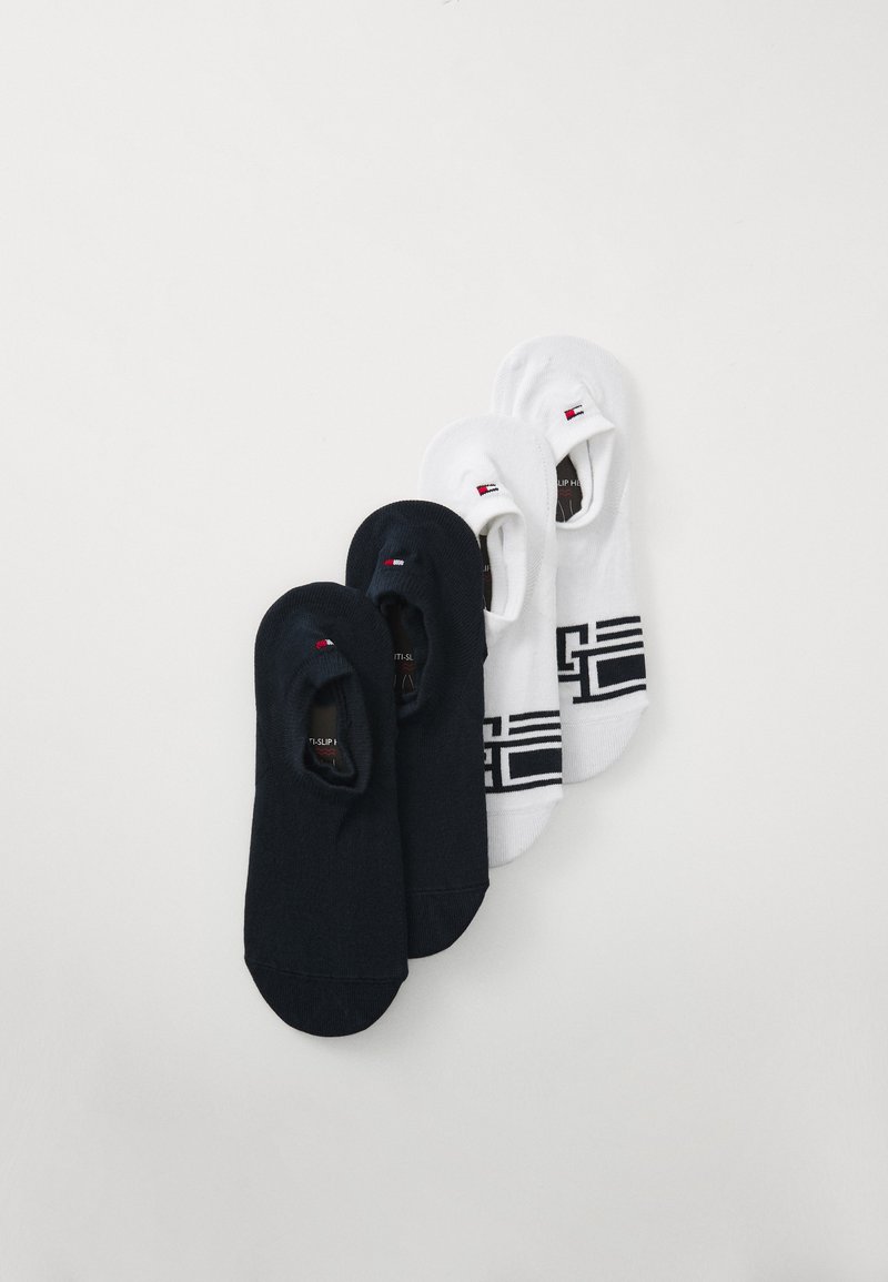 Two pairs of low-cut socks in navy and white. Navy pair is solid; white pair features a geometric black pattern and logo accent.