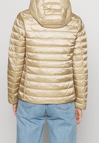 Béžová nafukovací bunda s horizontálním prošíváním, kapucí a lesklým povrchem. Vnitřní švy jsou viditelné; rukávy jsou přiléhavé a ribbované na manžetách.