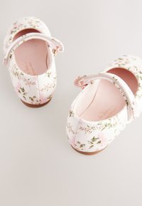 Chaussures Mary Jane à motif floral en blanc avec accents roses et verts. Dotées d'une bride ajustable et d'une texture lisse, avec une semelle plate.