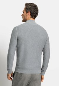 Maglione grigio a coste con colletto alto, maniche lunghe aderenti e orlo a bande solidi. Tessuto morbido, design semplice, senza loghi o motivi visibili.