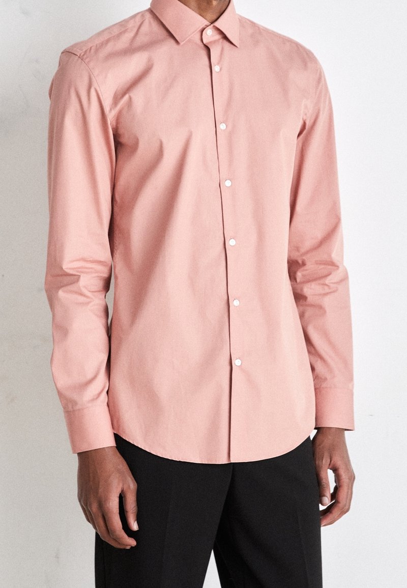 Katoenen lange mouw shirt in zachtroze, met een klassieke kraag, knopenlijst vooraan en een soepele textuur. Draag het met zwarte broek.