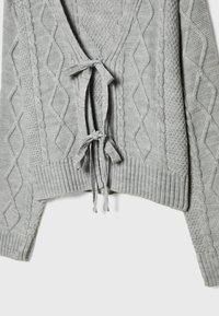 Cardigan gris clair en maille torsadée avec des motifs losange et corde, avec deux liens de fermeture à l'avant et des poignets et un bas côtelés.
