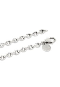 Zilveren kettingarmband met ovale schakels, kreeftsluitingen en een ronde tag gegraveerd met "GPH STUDIOS" op een witte achtergrond.