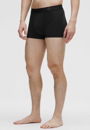 Bóxer negro con una tela lisa y elástica, que presenta una cintura ancha con un logo en la parte frontal, diseñado para un ajuste ceñido.