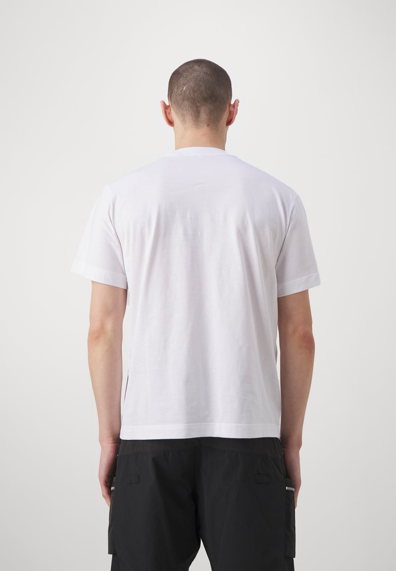 T-shirt bianca in cotone con maniche corte e colletto tondo, caratterizzata da un design semplice e una texture liscia, vista dal retro.