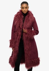 Bordeaux faux fur jas met een lange, luchtige kraag en manchetten, zachte suède textuur, knielange ontwerp en verborgen knoopsluiting.