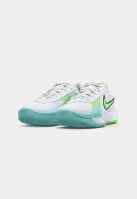 Et par hvide Nike sneakers med grønne accenter, lyseblå såler og sorte Nike swoosh-logoer på en hvid baggrund.