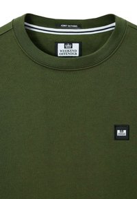 Sudadera de algodón color verde oliva con cuello redondo, una pequeña etiqueta negra con "WEEKEND OFFENDER" y un detalle de cuello interior a rayas.
