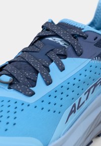 Chaussure de sport bleue avec une tige en mesh respirant, un embout renforcé, et des lacets bleu foncé avec des éclats clairs. Nom de la marque "ALTRA" visible.