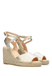 Sandalias de cuña metálicas doradas con punta abierta, tacón trenzado de yute y correas de tobillo entrelazadas. Textura suave y plantilla en color neutro.