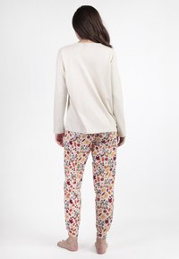 Top de manga larga beige combinado con pantalones de pijama coloridos que presentan un estampado de hojas y animales. Tela suave con un ajuste relajado.