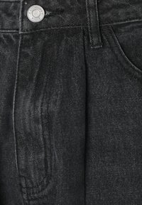 Pantalones de mezclilla negra con una superficie texturizada, cierre frontal con botón y bolsillos laterales. La tela tiene un ligero brillo y un diseño ajustado.