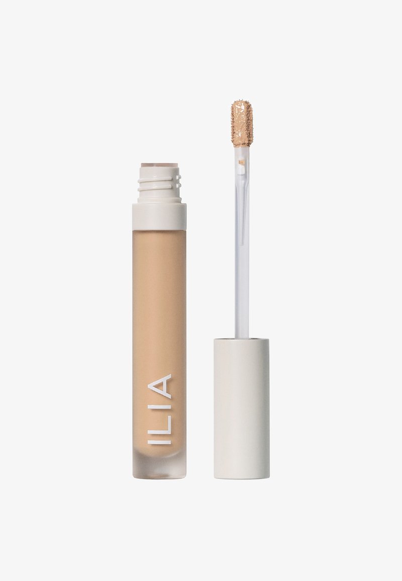 ILIA concealer i en transparent tub med en beige formula. Vit kork och applikator med rund spets och korta mjuka borst för precis applicering.