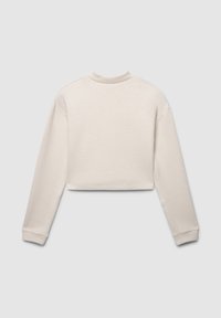 Krótka bluza z miękkiego, jasnego beżowego materiału, z długimi rękawami, okrągłym dekoltem i gładką fakturą. Szczegóły szwów są minimalne.