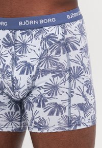 Blaue und weiße gemusterte Boxershorts mit einem Palmblatt-Design, ausgestattet mit einem blauen elastischen Bund, der "BJÖRN BORG" in Weiß zeigt.