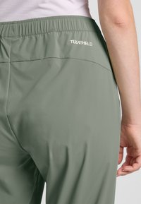 Lichtgroene, elastische broek met een gladde textuur. Beschikt over een TEXASHIELD-logo op de achterkant. Eenvoudig ontwerp zonder opvallende patronen.