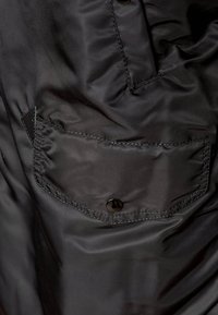 Schwarze Nylonjacke mit glatter Textur, zwei Seitentaschen mit Druckknopfverschlüssen und einem dezenten Glanz im Stoff.