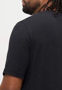 Μαύρο κοντομάνικο T-shirt από απαλό ύφασμα, με στρογγυλή λαιμόκοψη και καθαρές γραμμές, με λεία υφή και ουδέτερο σχέδιο.