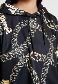Hooded sweatshirt in black fabric featuring a gold chain pattern, contrasting logo accents, and a textured drawstring.