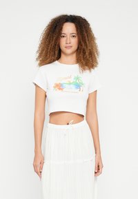 Witte cropped t-shirt met een kleurrijke afbeelding van bloemen, palmbomen en een zonsondergang. Gecombineerd met een witte laagjesrok met structuur.