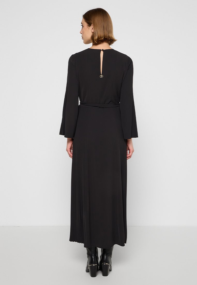 Abito lungo nero con maniche a campana lunghe e texture plissettata. Presenta una chiusura sul retro a chiave con un anello decorativo e una vita aderente.