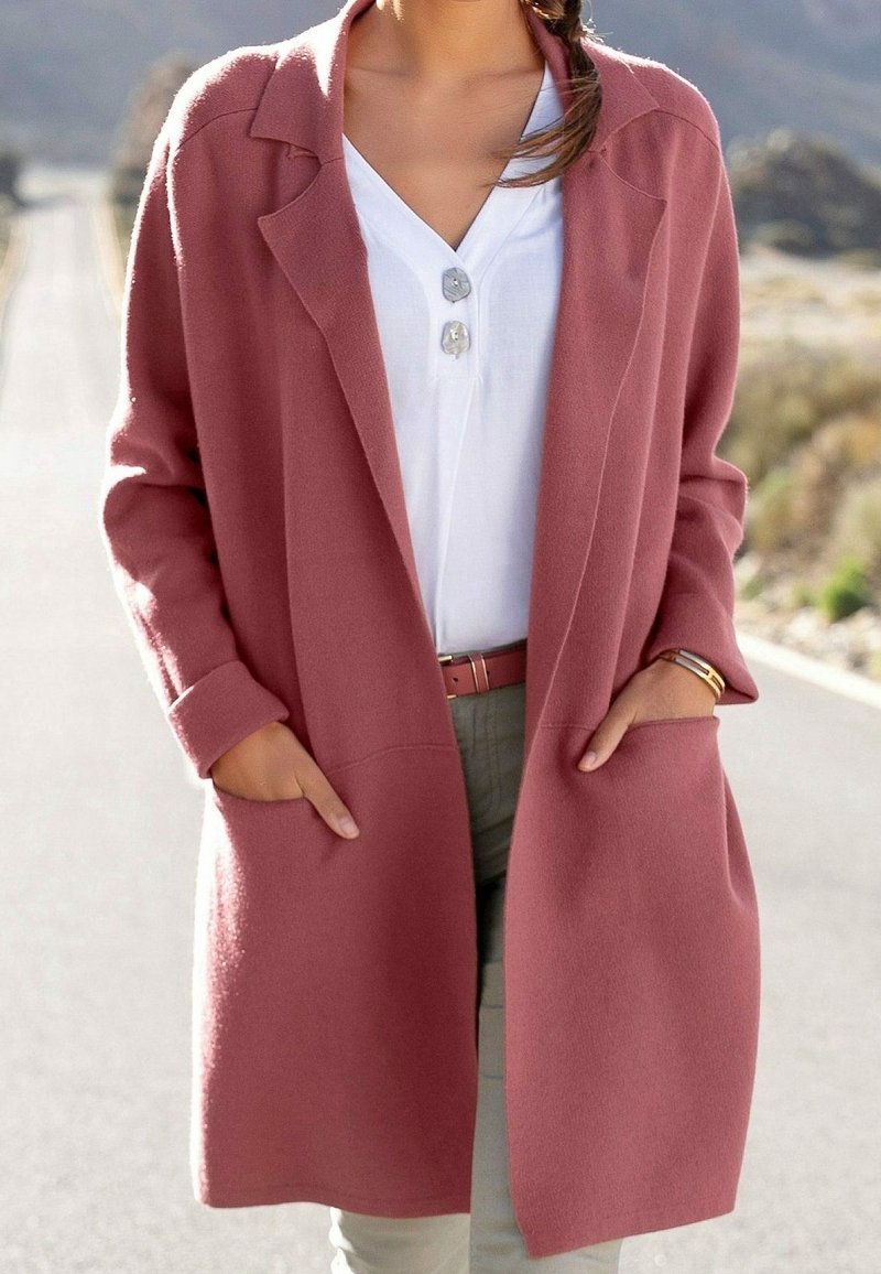 Lang vest in rozentinten van zacht materiaal, met een open voorkant, twee zijzakken en een losse pasvorm. Draagt over een wit shirt.