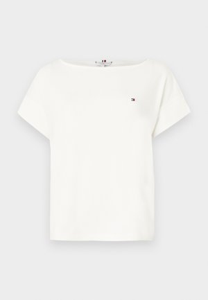 Tricou alb cu mânecă scurtă și guler rotund, cu un mic logo roșu, alb și albastru pe pieptul stâng, pe un fundal gri deschis.