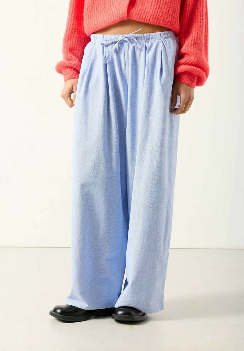 Svetlomodré široké nohavice s textúrovanou látkou, s elastickým pásom a sťahovacou šnúrkou. Kombinované s čiernymi topánkami.